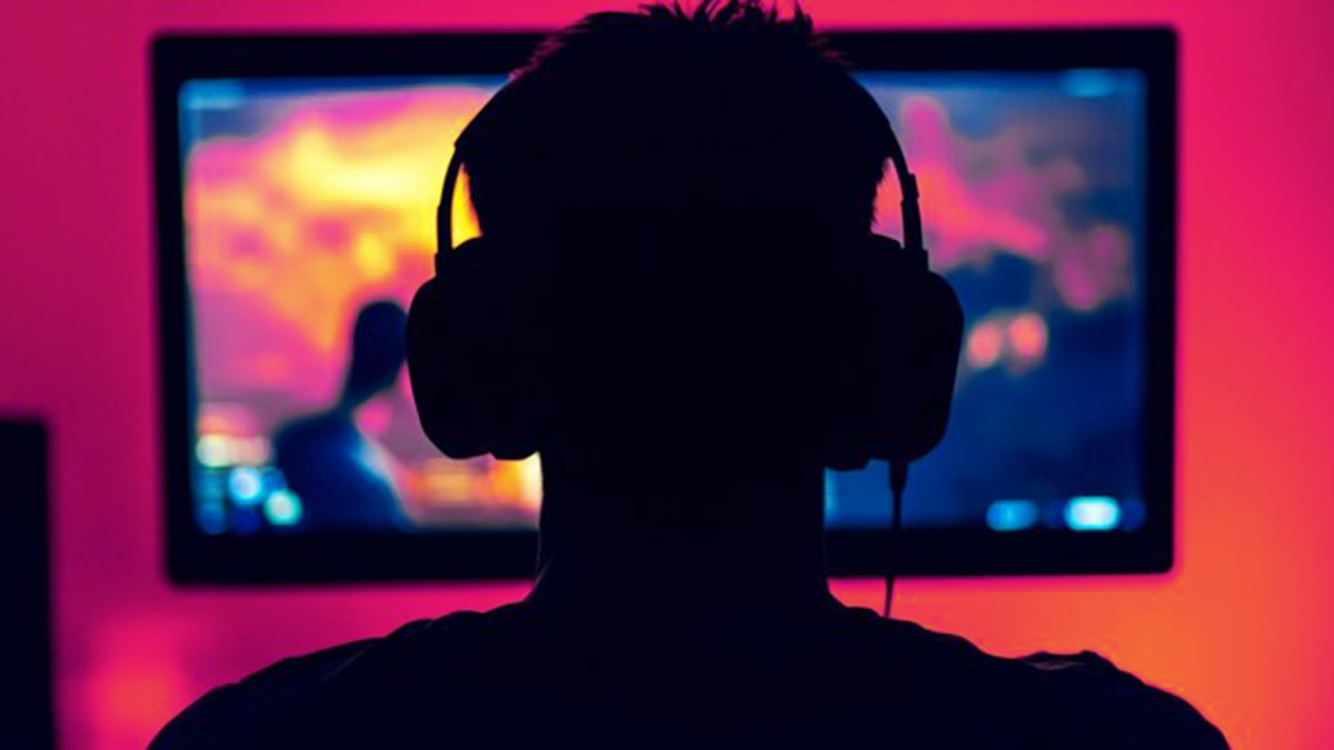 Image of a gamer in silhouette while playing an FPS browser game, with vibrant magenta toned wall.